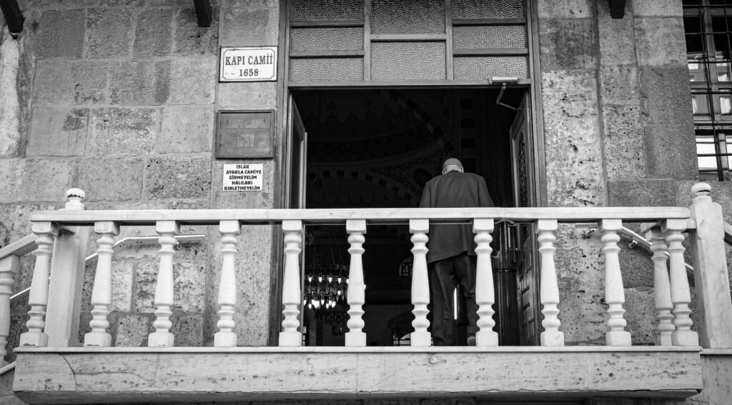 Schwarz-Weiß-Foto eines älteren Mannes, der in der Türkei eine Moschee betritt.